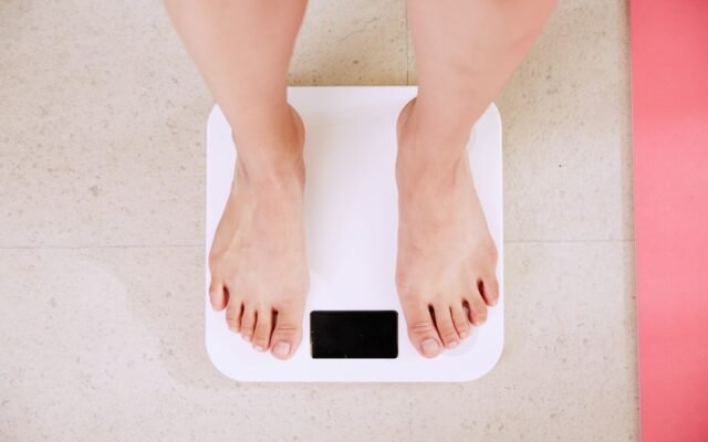 Person on scale reviewing ideal weight formulas and body frame size